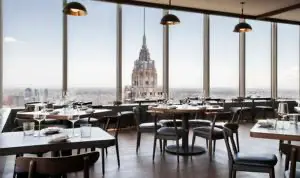 Intérieur d'un restaurant new-yorkais moderne avec de grandes baies vitrées offrant une vue imprenable sur l'Empire State Building.