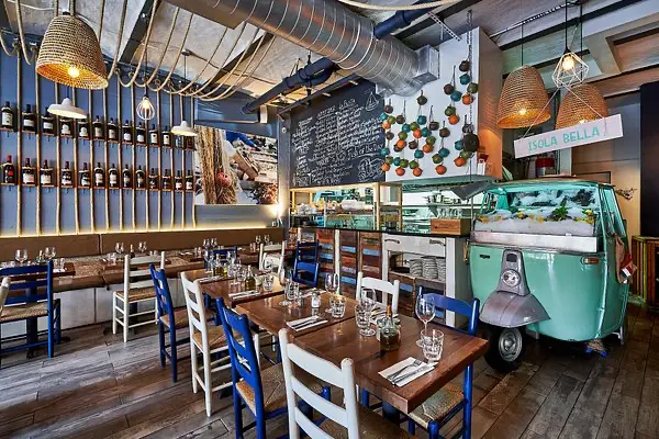 Intérieur d'un restaurant new-yorkais à Harlem avec une décoration méditerranéenne, des chaises colorées, un tableau noir pour le menu et une petite camionnette rétro utilisée pour l’exposition des produits.