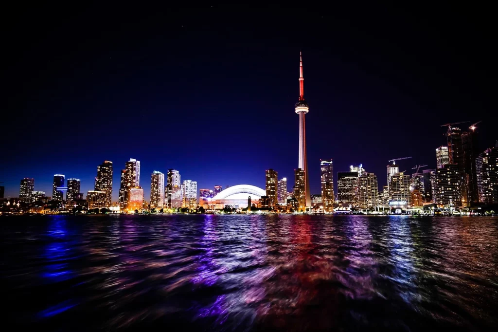 Skyline de Toronto avec la tour CN et des immeubles modernes, reflétée dans le lac Ontario sous un ciel nuageux.