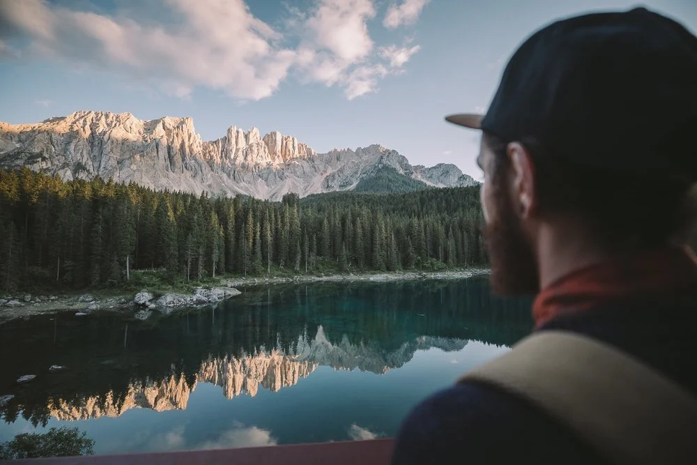 Une personne regardant un lac, une forêt avec une chaine de montagne au loin